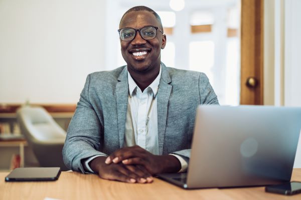 Black higher ed professional at desk, smiling at camera